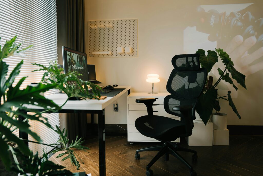 Cozy and modern home office setup with a stylish ergonomic chair, plants, and a desktop monitor.