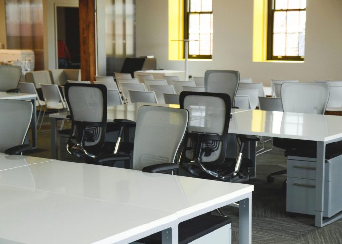 Spacious open office workspace with desks, chairs, and natural lighting.